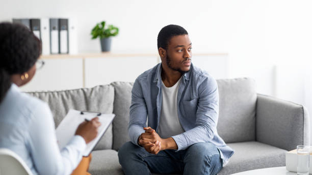 istock Depressed black man consulting psychologist, sitting on couch deep in thought, panorama 1328840015