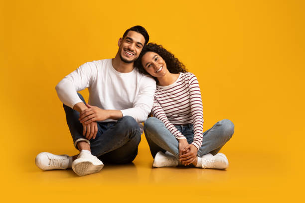 Romantic young middle eastern couple sitting on floor over yellow background