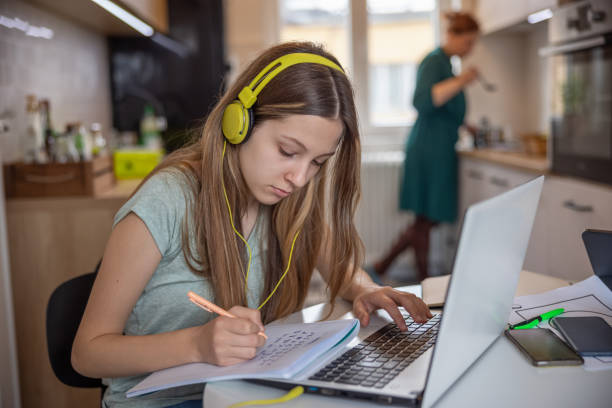 istock Teenage girl using laptop for remote learning and taking notes, mother working at home 1328841402