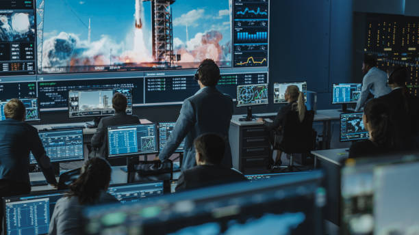 미션 컨트롤 센터의 사람들 그룹은 성공적인 우주 로켓 발사를 목격합니다. 비행 제어 직원은 전면 컴퓨터 디스플레이에 앉아 승무원 임무를 모니터링합니다. 팀이 일어서서 지켜봅습니다. - control room audio 뉴스 사진 이미지