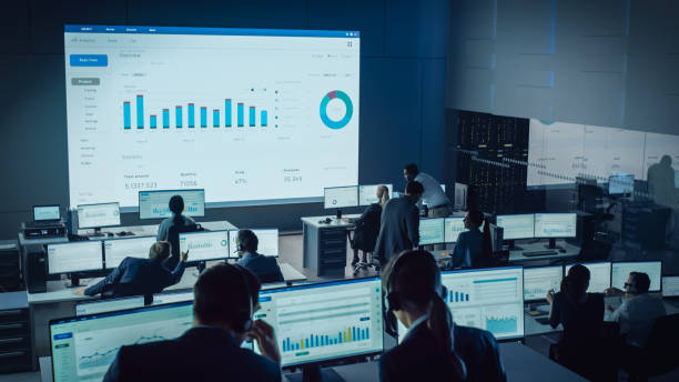 istock Professional Traders Working in a Modern Monitoring Office with Live Analytics Feed on a Big Digital Screen. Monitoring Room with Brokers and Finance Specialists Sit in Front of Computers. 1328842080
