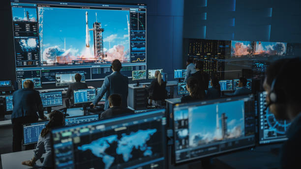 istock Group of People in Mission Control Center Witness Successful Space Rocket Launch. Flight Control Employees Sit in Front Computer Displays and Monitor the Crewed Mission. Team Stand Up and Watch. 1328842093