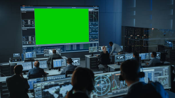 duży zielony ekran poziome mock up w mission control center pokój z dyrektorem lotu i innych kontrolerów pracujących na komputerach. zespół inżynierów pracuje w pokoju monitoringu pełnym wyświetlaczy. - control room audio zdjęcia i obrazy z banku zdjęć