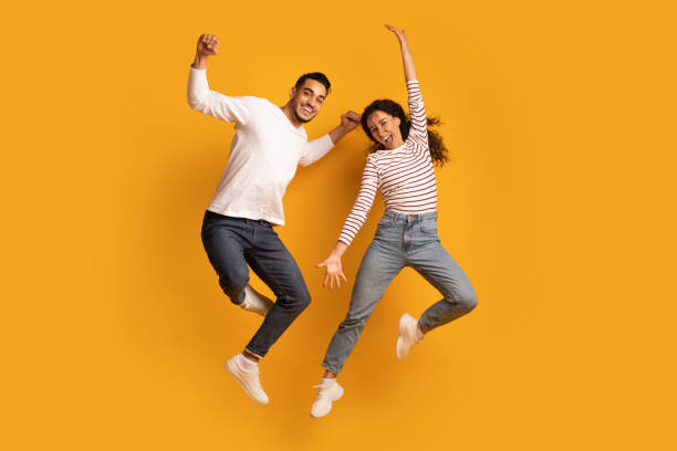 cheerful active arab couple jumping in air over yellow background - hop imagens e fotografias de stock