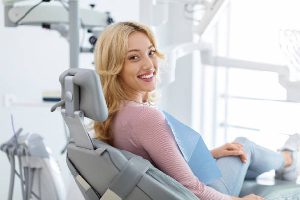 joven sonriente y relajada sentada en una silla dental - salud dental fotografías e imágenes de stock