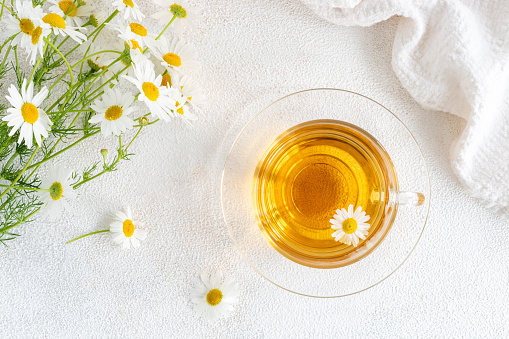 Top view of chamomile tea in a transparent mug with natural small chamomile flowers