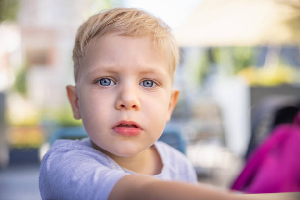 Headshot of blond toddler with blue eyes playing outside and looking at camera