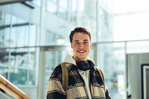 Young man standing at stairs and smiling in college. Boy in casual wear looking at camera while at high school campus.