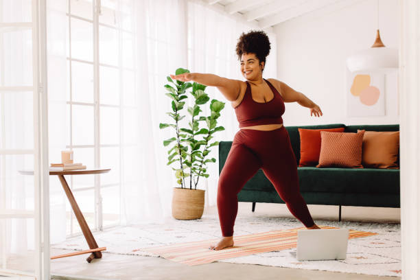Healthy woman doing yoga at home Full length of healthy woman exercising at home watching online video on laptop. Beautiful female in sports wear doing yoga. warrior position stock pictures, royalty-free photos & images