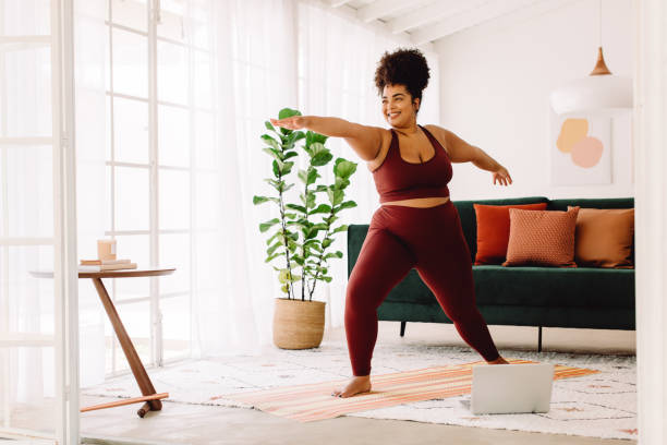 Healthy woman doing yoga at home Full length of healthy woman exercising at home watching online video on laptop. Beautiful female in sports wear doing yoga. relaxation exercise stock pictures, royalty-free photos & images