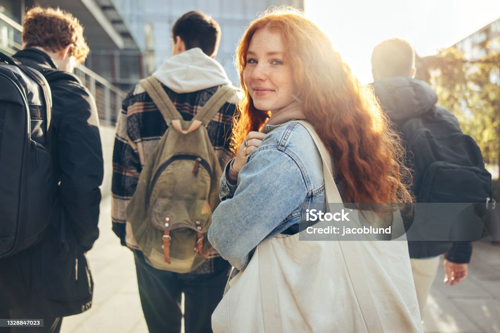 Female student going for class in high school Female student glancing back while going for a class in college. Girl walking with friends going for class in high school. Teenager Stock Photo