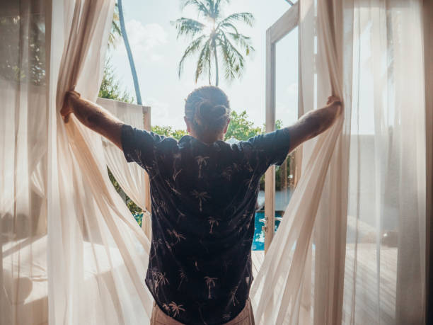 istock Man opening curtains in hotel room at sunrise 1328850080