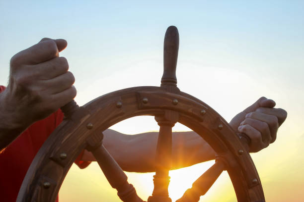 A man controls the yacht, hands on the steering wheel, handwheel on sky background stock photo