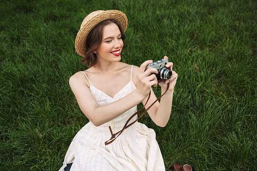 Close-up of portrait of one beautiful young woman with sun hat standing, holding and smelling bouquet  of wildflowers, enjoying summer sunset over blooming meadow, feeling free, relaxed and happy in nature, front view