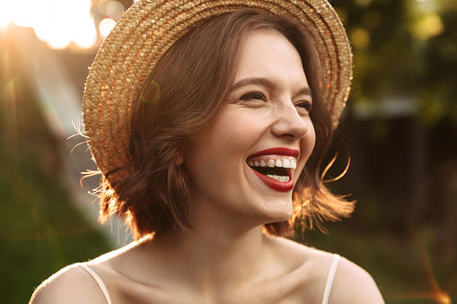 Close up image of Laughing woman in dress and straw hat looking away while posing outdoors