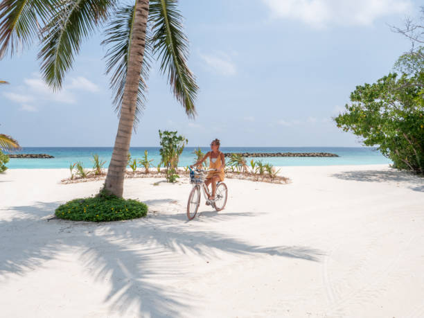 giovane donna in bicicletta sulla spiaggia tropicale - luxury hotel palm tree lush foliage asia foto e immagini stock