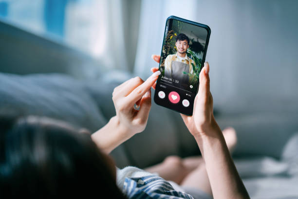 mujer joven asiática acostada en el sofá de casa, utilizando una aplicación de citas en línea en el teléfono inteligente, en busca de amor en internet. redes sociales. citas por internet. relación de pareja. concepto de amor - internet dating fotografías e imágenes de stock