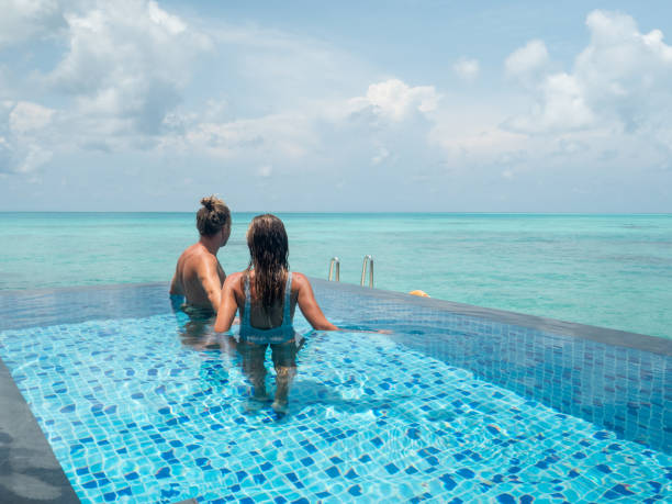 istock Couple swim in infinity pool over tropical lagoon 1328853728
