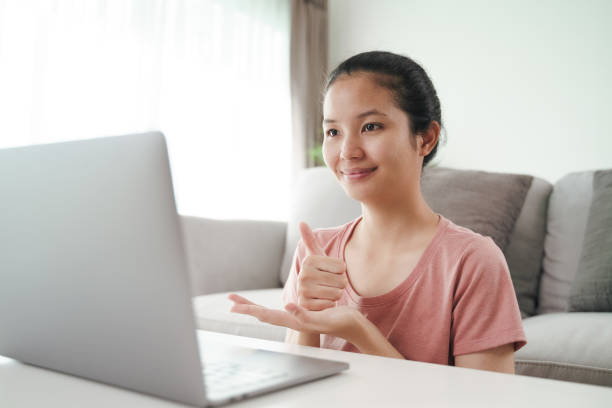 Young Asian woman deaf disabled using laptop computer for online video conference call learning and communicating in sign language.