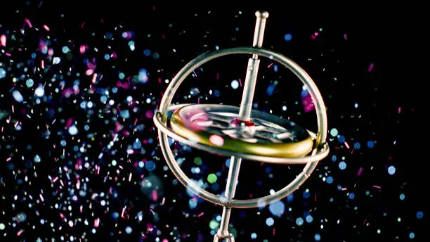 Close-up metal gyroscope spinning in a colourful glitter dust against black background.