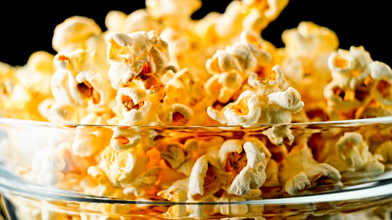 Host movie premieres with your buddies and delicious snacks. Side view photograph of tabletop featuring mouthwatering popcorn in striped boxes against red wall, providing space for movie advertisement