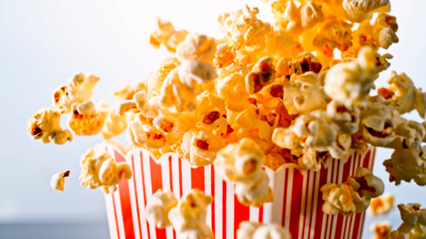 Popcorn overflowing from red striped carton Close up of overflowing popcorn from red striped carton against blue background. overflowing stock pictures, royalty-free photos & images