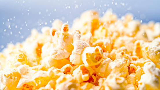 Close- up of salt sprinkling over popcorn against blue background.