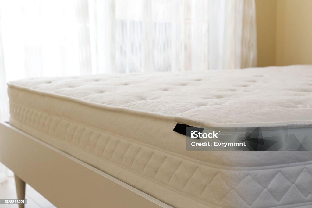 New white mattress. White orthopedic mattress top side surface pattern on unmade bed in the bedroom. Hypoallergenic foam mattress for proper spinal alignment and pressure point relief. Background, copy space, close up. Mattress Stock Photo