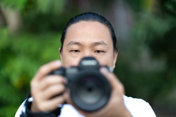 istock Focus on the Asian man face that he holds the blur Medium Format Camera in his hand and prepare to shoot in front of him. 1328856972