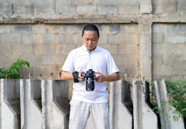 istock Asian Thai - Chinese professional camera man posts and check image shot via liveview behind Medium format Mirrorless camera with construction background. 1328856975