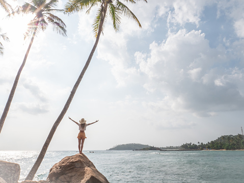 Cheerful woman standing on rocky hill above the sea looking out at nature