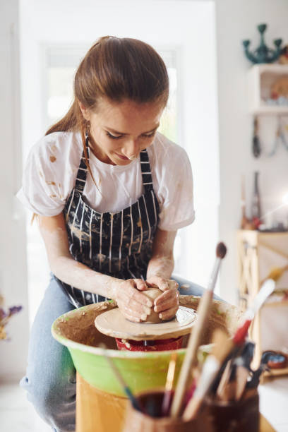 istock Young female ceramist working by using pottery wheel indoors and making handmade clay product 1328866607