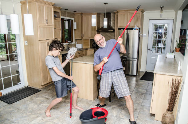Boy playing with a mop with father Boy dancing with a mop and father playing guitar with broom while doing chores in the kitchen father and son guitar stock pictures, royalty-free photos & images