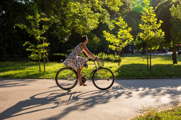 istock Young summer dressed woman cycling down park lane 1328868579