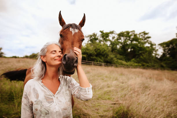 bella donna matura godendo a occhi chiusi la sua cavalla araba marrone nella natura libera - cavallo foto e immagini stock