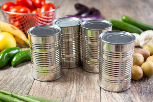 A view of several blank label canned food, with several varieties of produce in the background.
