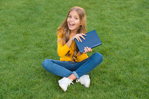 write childhood memories. kid read book in park. happy little girl study on holiday. kid beauty fashion. teen girl inspired with new book. relax on green grass. spring leisure time. happy childhood.