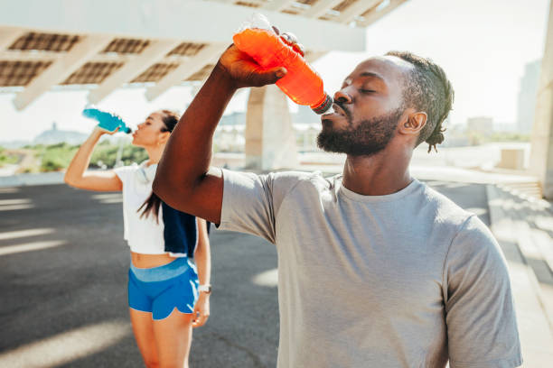 Sporty runners couple drinking energy drink after running Sporty runners couple drinking energy drink after running. Multi ethnic couple drinking isotonic drink. energy drink stock pictures, royalty-free photos & images
