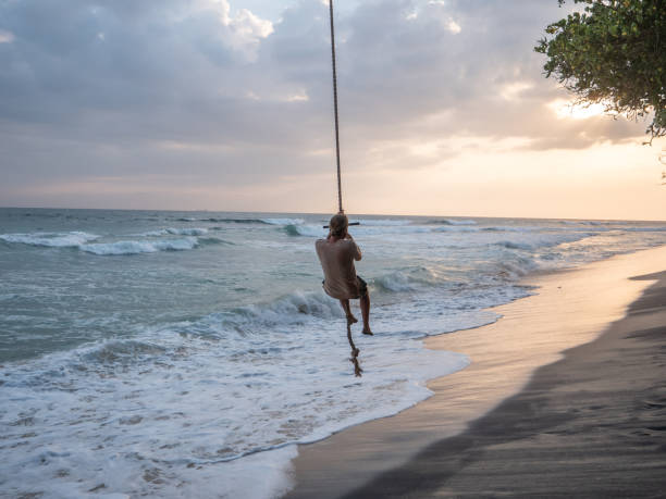 istock Man plays on rope swing above sea 1328871098