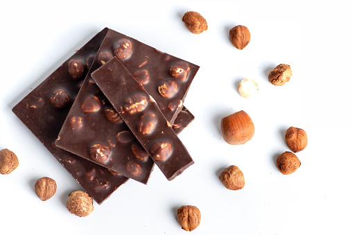 Sweet and tasty hazelnut chocolate pieces with organic hazelnuts on a pile isolated on white background