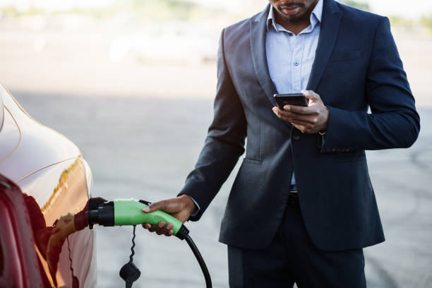 istock African man charging electric car and using mobile 1328876542