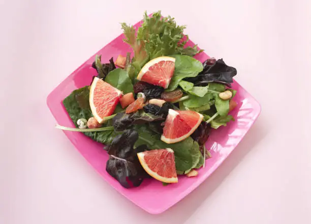 Vegetable,sliced Orange fruit,raisin,and beans put in pink dish,salad mixed,on pastel background