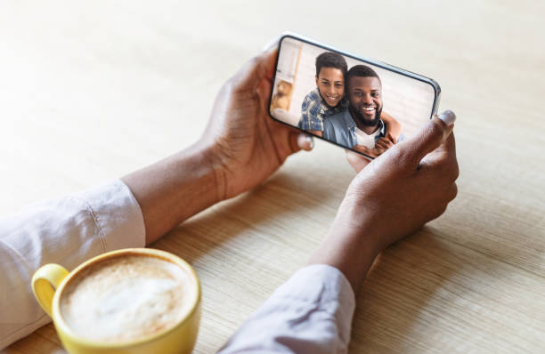 istock Young black woman speaking to her husband and son on webcam, using online video chat on smartphone at table in cafe 1328878932