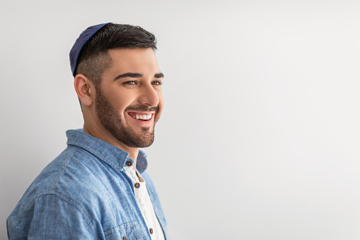 Happy Person. Closeup portrait of handsome cheerful israeli guy posing at studio, smiling and looking aside, wearing yarmulke, posing isolated on light background wall, copy free space, advert banner