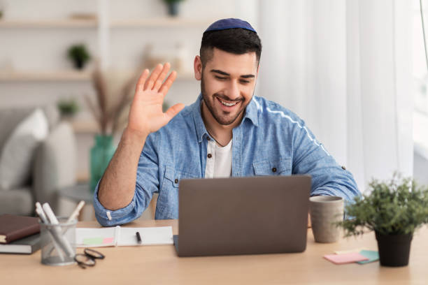 istock Smiling israeli man working on laptop waving hand 1328880740
