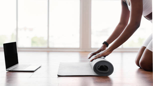 giovane donna nera srotolare tappetino yoga sul pavimento vicino al pc - unrolling foto e immagini stock