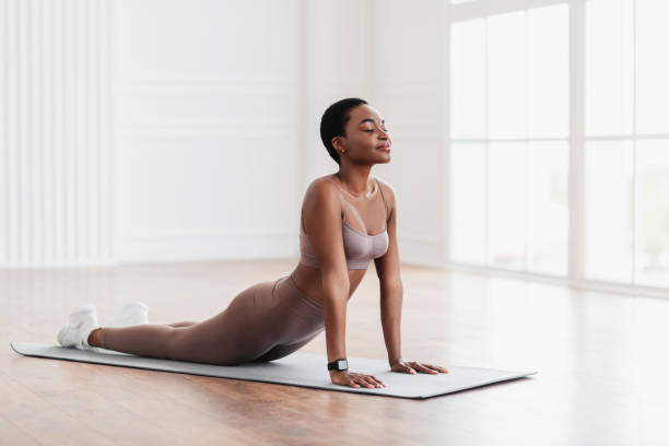 молодая чернокожая женщина, растягивающаяся назад на коврике, поза кобры - stretching yoga exercise mat women стоковые фото и изображения