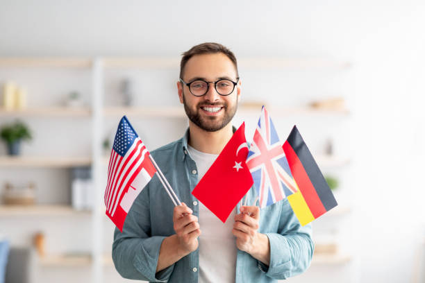 istock Handsome young guy holding bunch of diverse flags and smiling at camera indoors 1328883122
