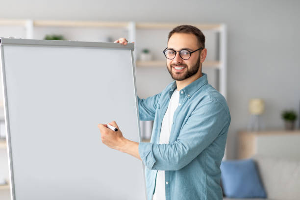 istock Foreign languages tutor giving online class, pointing at empty blackboard with mockup, having video call with students 1328883340