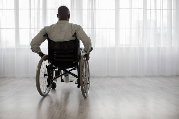 persona discapacitada se sienta en silla de ruedas contra la ventana - parálisis fotografías e imágenes de stock